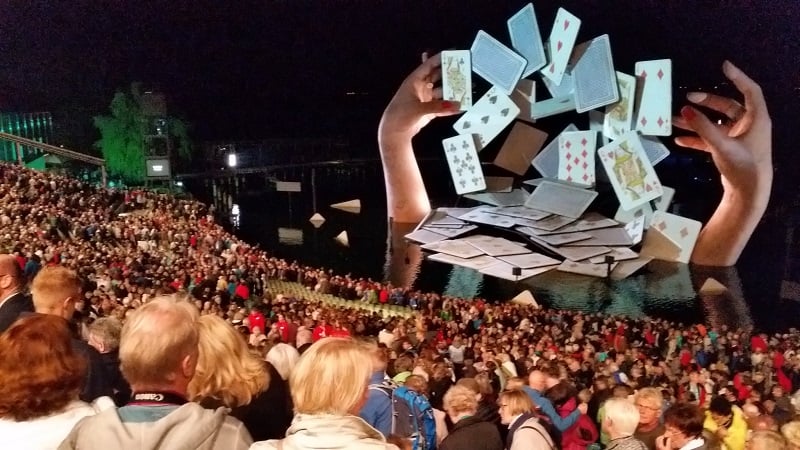 Giant hands shuffling cards at theatre festival stages.