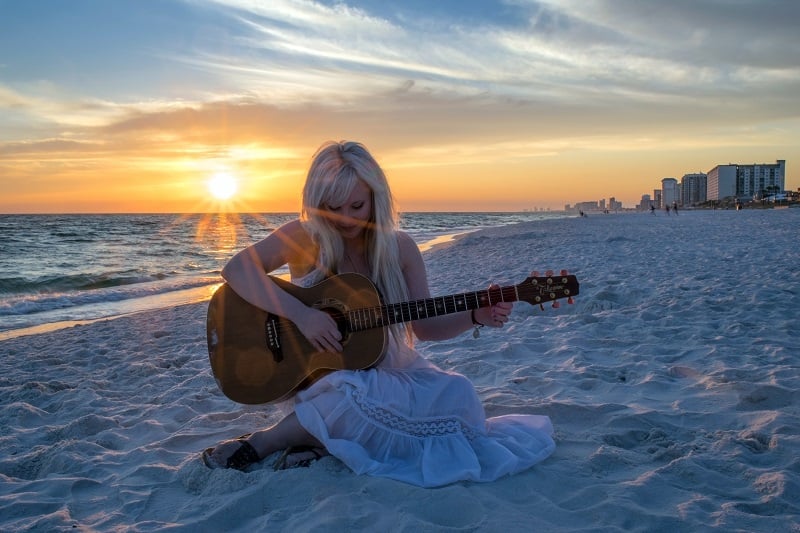 A woman on the beach playing her guitar.