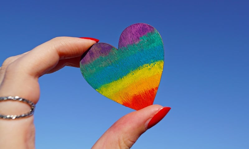 Fingers holding a wooden heart.