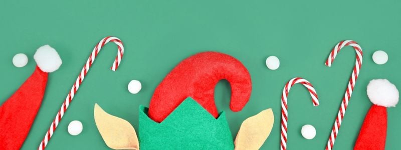 Elf hat, candy canes and Santa hat on a green background.