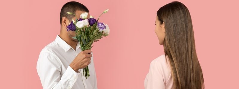 A man giving flowers to a woman with a pink background.