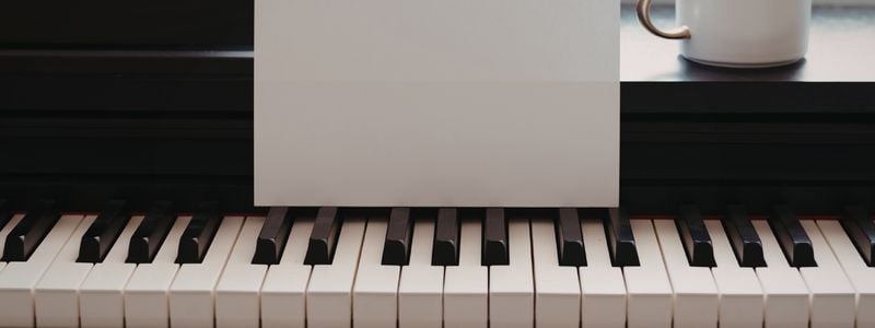 A piano with a blank sheet of paper and a mug.