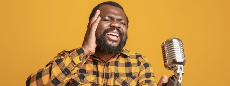 A man singing into a microphone with a yellow background.