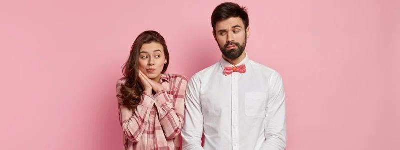 A couple looking at each other awkwardly with a pink background.