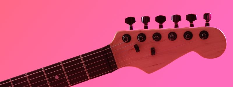 A closeup of a pink guitar with pink background.