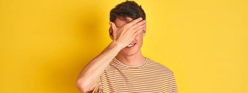 A teen hiding his face in front of a yellow background.