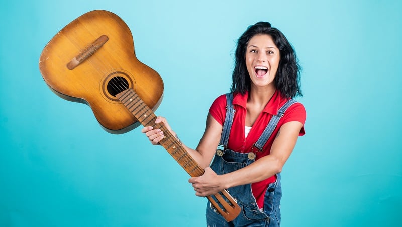 A silly woman waving a guitar in the air.