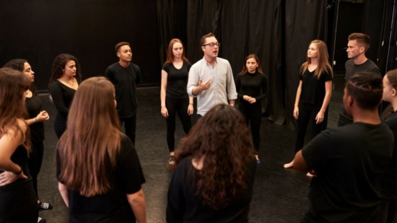 A drama teacher surrounded by students.