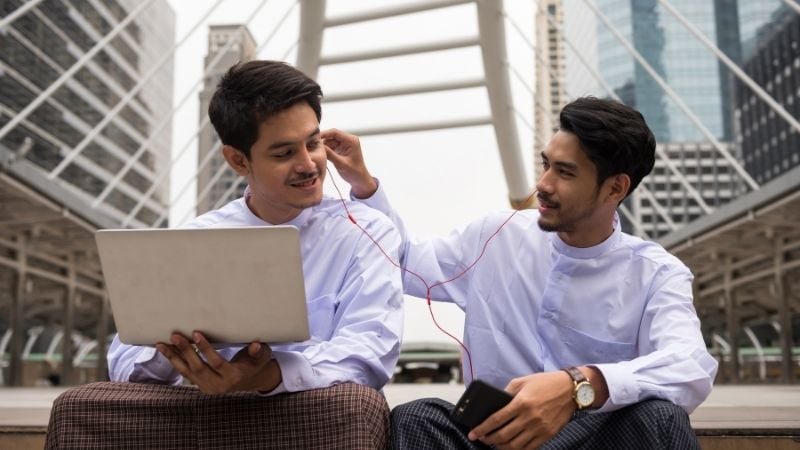 Two young men sharing headphones.