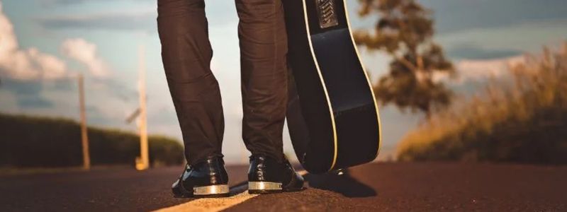 A man standing on the road with a guitar.