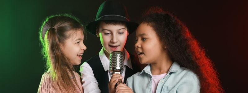 Three kids with a microphone on stage.