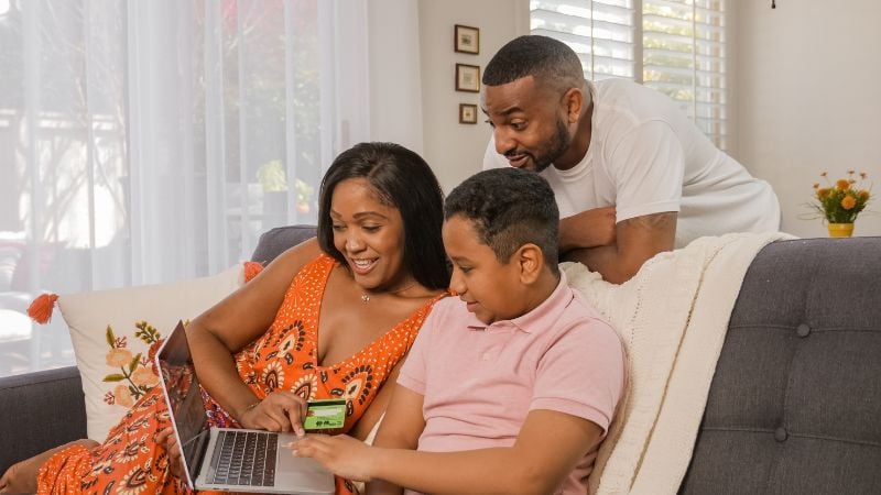 A family of three sitting around a laptop.