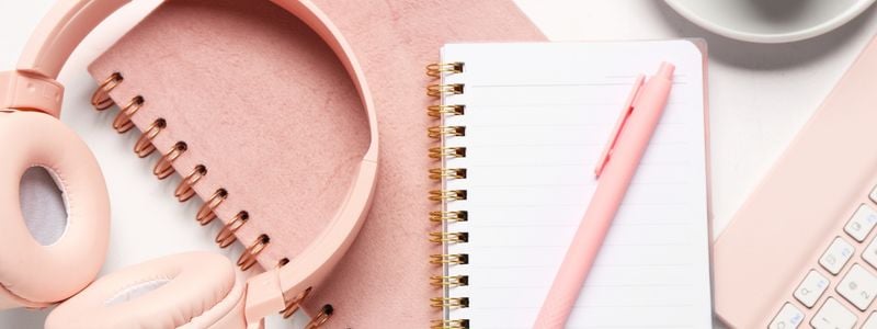 A blank notebook, pink headphones, and a pink pen.