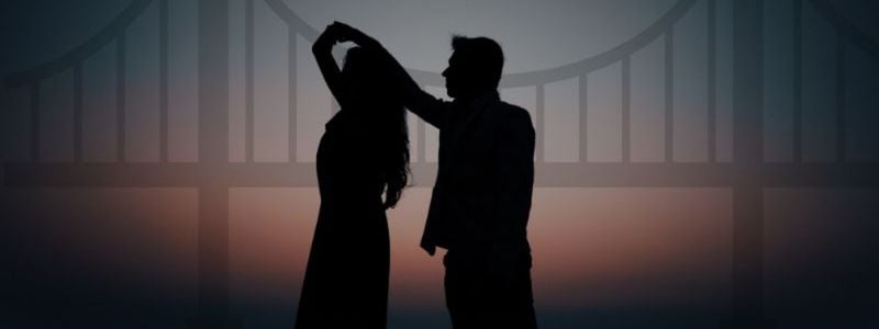 A silhouette of a couple dancing in front of a bridge.