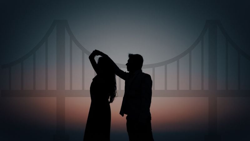 A silhouette of a couple dancing in front of a bridge.