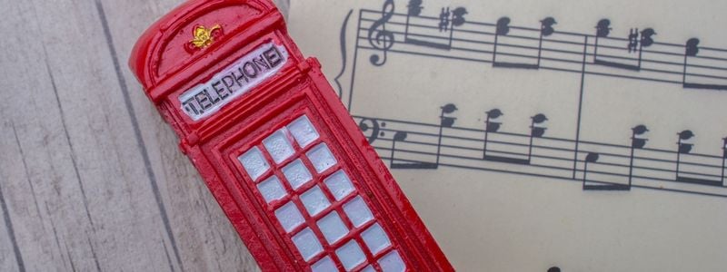 A miniature telephone booth toy lying on top of music notes.
