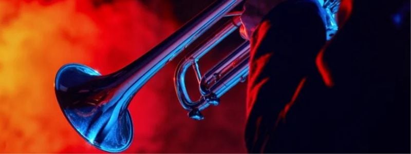 A brass instrument being played with a fiery red background.