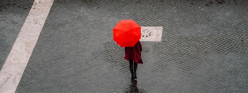 A woman on the street with a red coat and umbrella.