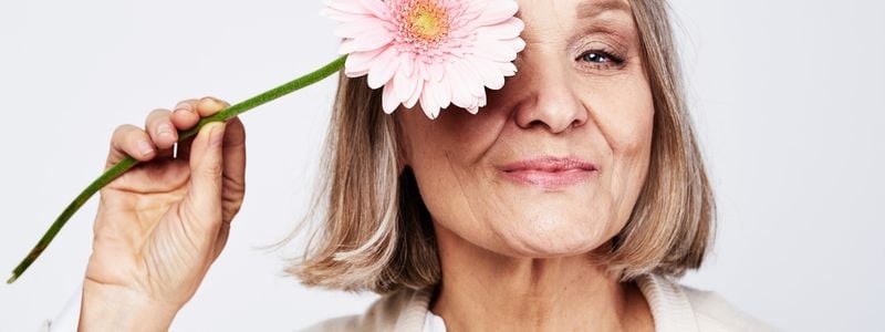 An older woman holding a flower.