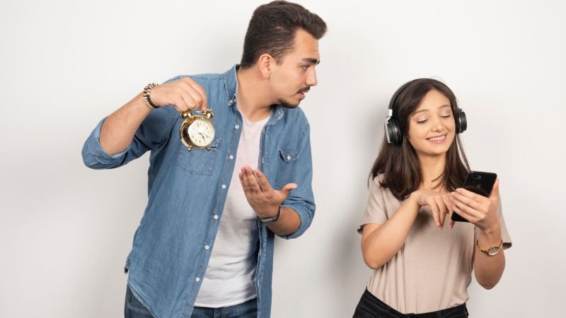 A man holding up a clock and a young woman with headphones on.