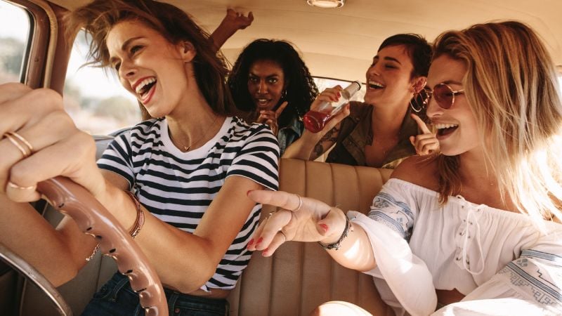 Four women singing in the car on a road trip.
