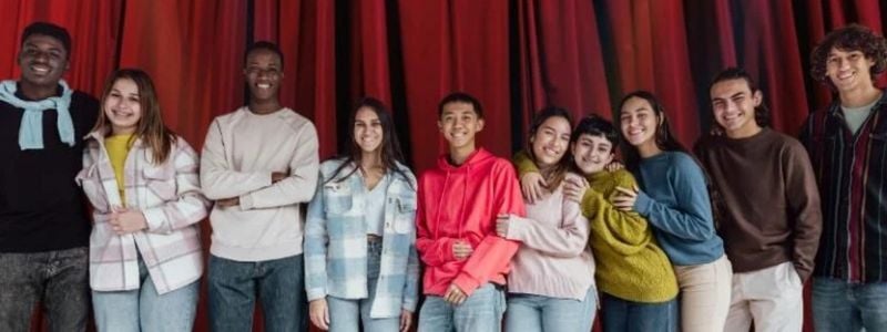 A group of teens standing in front of a stage curtain.
