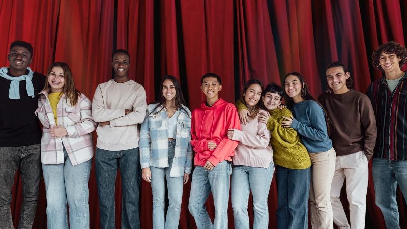 A group of teens standing in front of a stage curtain.
