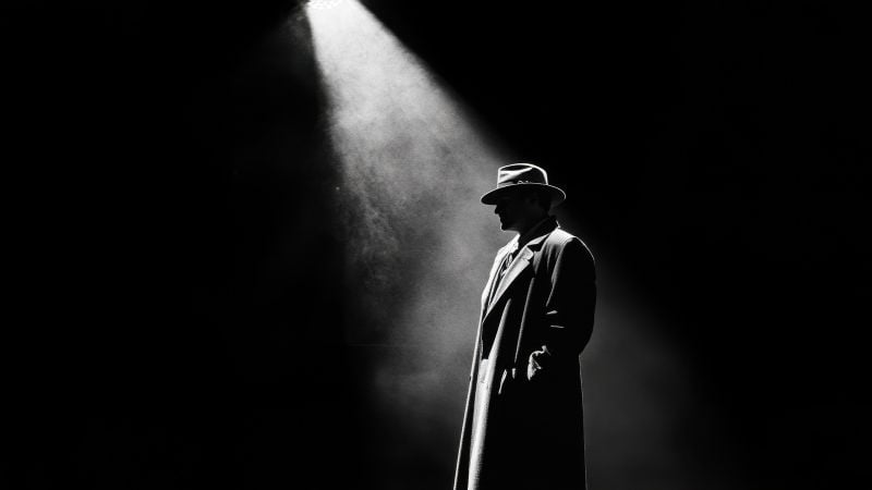 A detective in the spotlight on a dim stage.