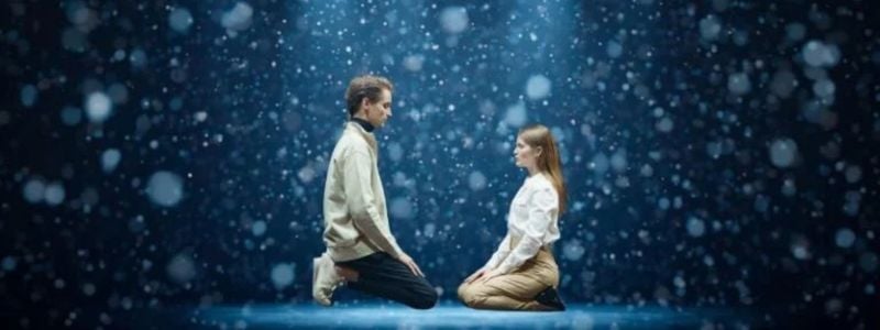 Two actors kneeling on a snowy stage.