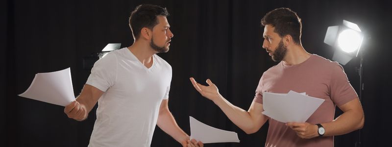 Two male actors with scripts on stage.
