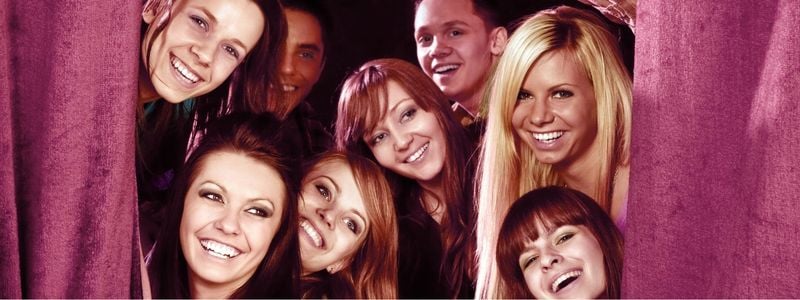 Eight actors poking their heads out from the stage curtain.