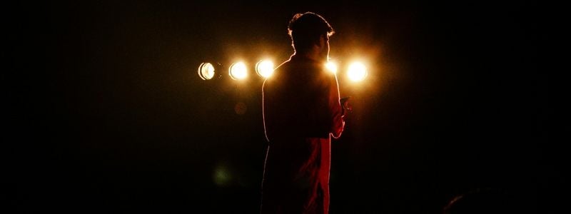 The back of a solo performer on stage with lights.