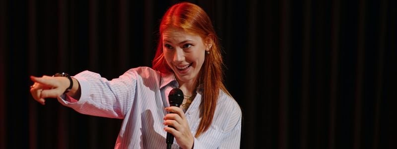 A comedian on stage pointing her fingers at the audience.